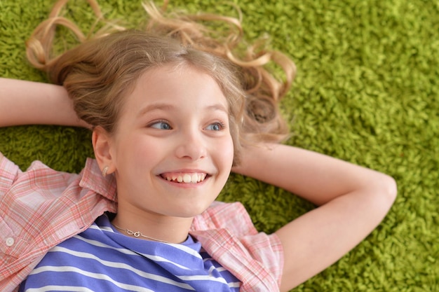 Divertida niña sonriente acostada sobre una alfombra verde