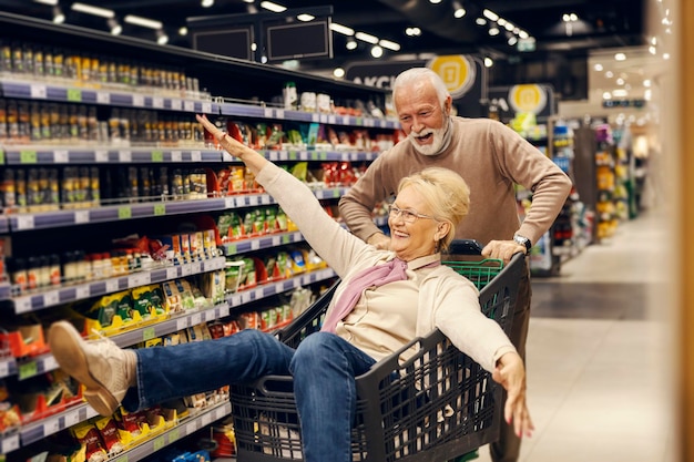 Una divertida pareja de ancianos conduce un carrito de compras en el supermercado