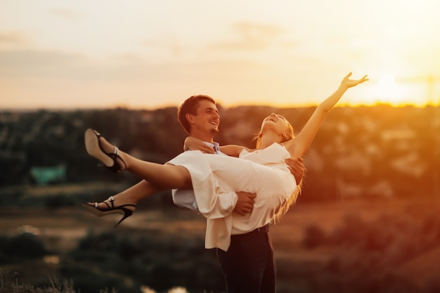 Divertida pareja feliz divirtiéndose al aire libre. Guy levantó a su amante en sus brazos, la niña se ríe.