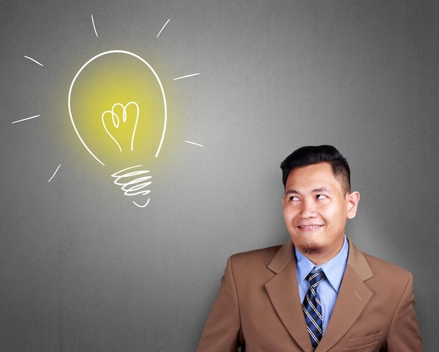 divertido empresario asiático sonriendo pensando y mirando hacia el lado con el icono de la lámpara de la bombilla idea