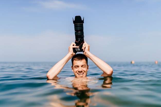 Divertido fotógrafo con una cámara en la cabeza está hasta el cuello en el agua