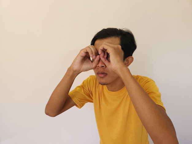 Divertido hombre asiático que mira a escondidas obvio en camiseta amarilla aislado sobre fondo blanco