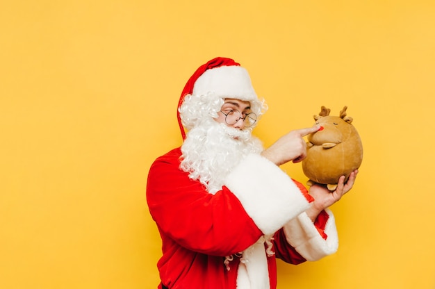 Divertido y lindo Papá Noel sostiene un reno de peluche en su mano