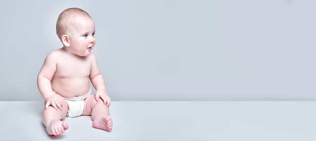 Divertido niño dulce niño sentado en el piso blanco en pañales y mirando hacia el lado en el espacio de copia aislado