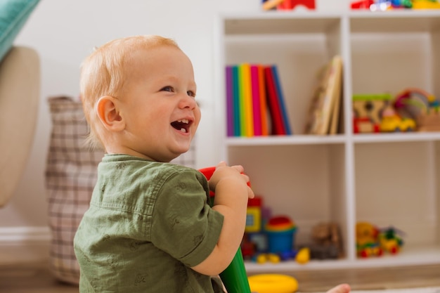 El divertido niño pequeño sentado en medio de la habitación. Juega con el juguete y sonríe.