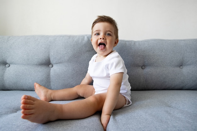 Divertido niño sano feliz de un año sentado en el sofá en casa ojos bonitos niños juegan y niño ...