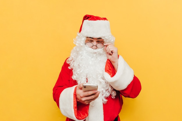 Divertido Santa Claus usando un teléfono sobre un fondo amarillo