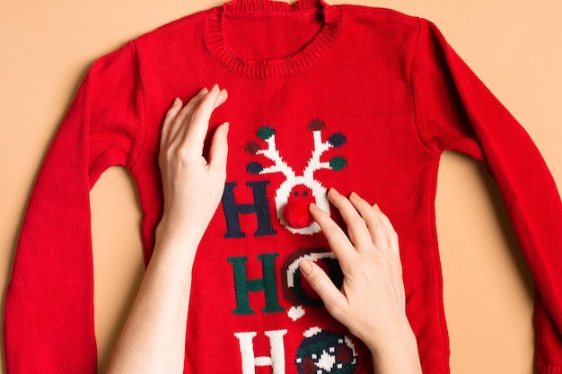 Divertido suéter navideño con manos femeninas preparando ropa para año nuevo