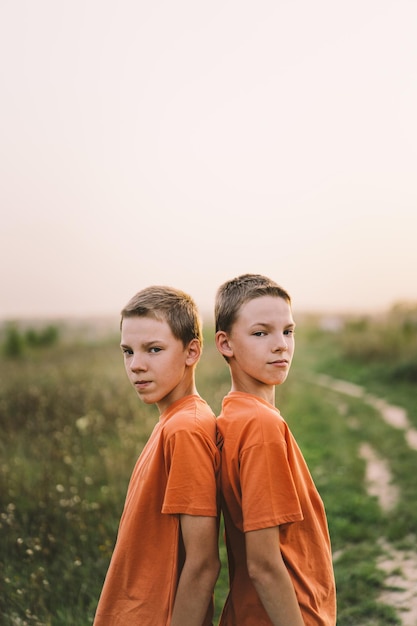 Divertidos hermanos gemelos con camiseta naranja jugando al aire libre en el campo al atardecer Estilo de vida de niños felices