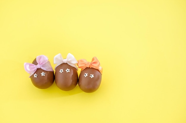 Divertidos huevos de chocolate decorados con lazos de colores sobre fondo amarillo Diy de Pascua para niños