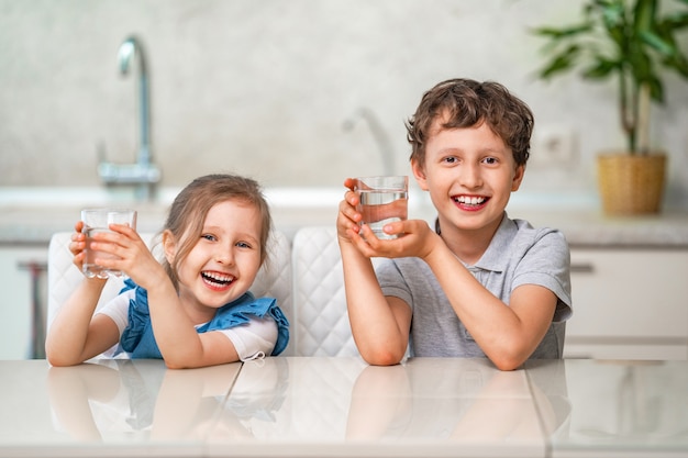 Divertidos niños beben agua en la cocina en casa