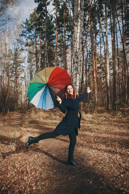 Divertimentos de mulher com um guarda-chuva colorido caminha na floresta.