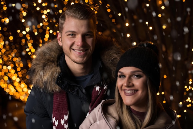 Divertindo-se juntos em um jovem casal alegre de fadas de Natal está passeando se divertindo vestidos quentes olhando um para o outro e rindo