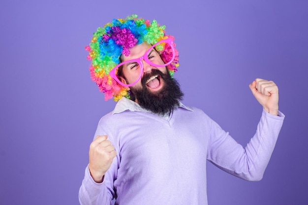 Divertirse Diversión de vacaciones y concepto de carnaval Hombre barbudo usa peluca colorida y gafas divertidas sobre fondo violeta Payaso y circo Diversión de fiesta Disfruta de estar loco Siéntete libre de expresarte