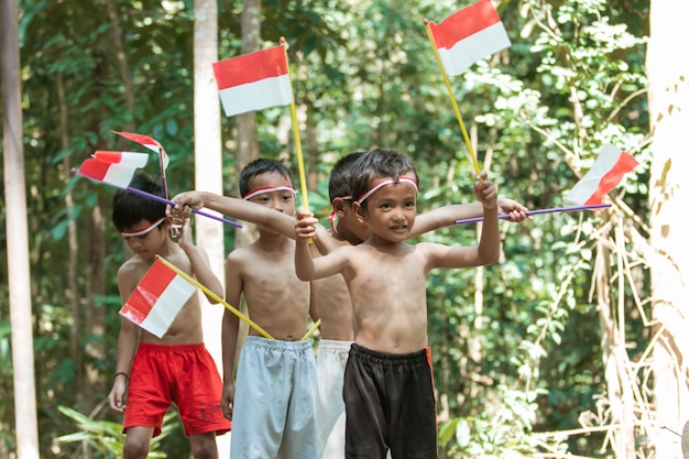 Divirtiéndose grupo de niños de pie sin ropa cuando sostienen la pequeña bandera roja y blanca y levantan la bandera