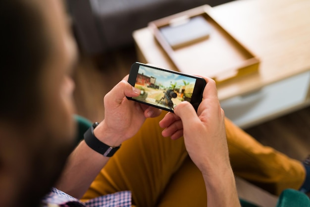 Divirtiéndose. Joven jugando un videojuego en línea en su teléfono inteligente