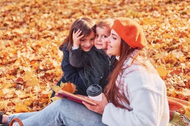 Divirtiéndose Madre con su pequeño hijo e hija está en el parque de otoño