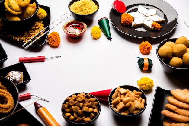 Foto diwali dulces y bocadillos dispuestos en un grupo con diya o lámpara de aceite, flores y galletas de fuego o patakhe sobre superficie cambiante, enfoque selectivo