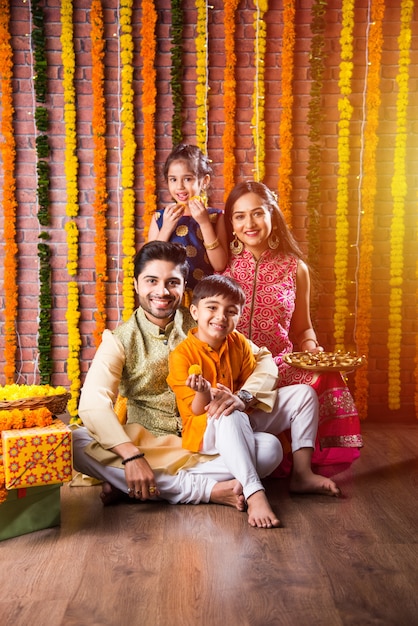 Diwali- oder Rakshabandhan-Feier - Indische junge vierköpfige Familie, die das Deepavali- oder Bhai-Dooj-Festival mit süßem Laddoo, Öllampe oder Diya und Geschenkboxen feiert, Essen isst oder Selfies macht