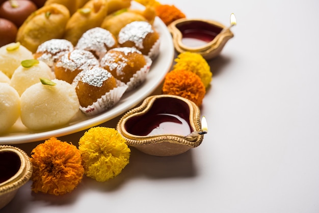 Diwali Rangoli hecho con Diya o lámpara de aceite, flores y plato lleno de Gulab Jamun, Rasgulla, kaju katli, morichoor o Bundi Laddu, Gujiya o Karanji