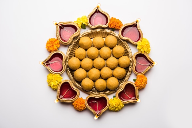 Diwali Rangoli mit Diya, Blumen und Besan Laddu oder Laddoo arrabged über weiße Szene, selektiver Fokus