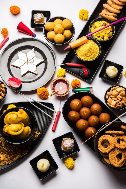 Diwali-Süßigkeiten und Snacks in einer Gruppe mit Diya oder Öllampe, Blumen und Feuerwerkskörpern oder Patakhe über stimmungsvoller Oberfläche, selektiver Fokus selective