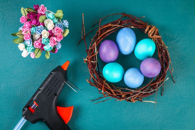 Diy guirnalda de Pascua de ramitas, huevos pintados y flores artificiales sobre un fondo verde.