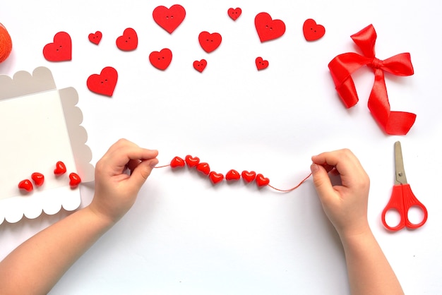 DIY kids maneja una cadena de corazones de cuentas rojas en una cadena para la pulsera del día de San Valentín. decoración de bebé hecha a mano. concepto de artesanía.