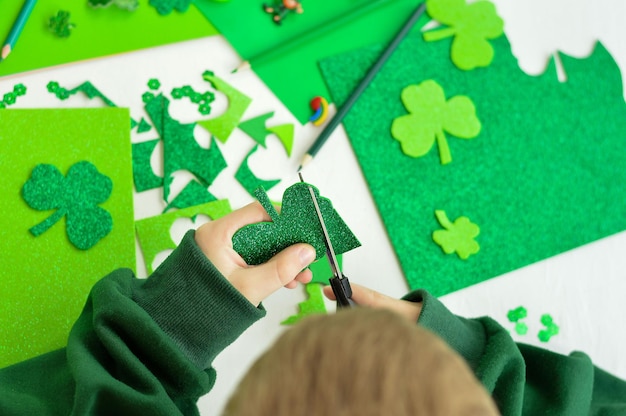 DIY StPatricks Day decor Ein Junge schneidet mit einer Schere Bastelkarte aus glänzendem grünem Papier Selektiver Fokus