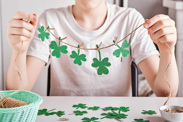 DIY StPatricks Day Dekor Fröhlicher Junge macht Girlande aus glänzendem grünem Papier Selektiver Fokus