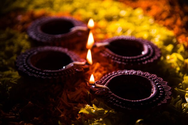 Diya tradicional o lámpara de aceite encendida en coloridos rangoli hechos de pétalos de flores, en el festival de luces llamado diwali o deepawali, enfoque selectivo