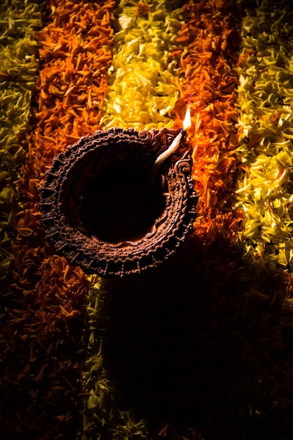 Diya tradicional o lámpara de aceite encendida en coloridos rangoli hechos de pétalos de flores, en el festival de luces llamado diwali o deepawali, enfoque selectivo