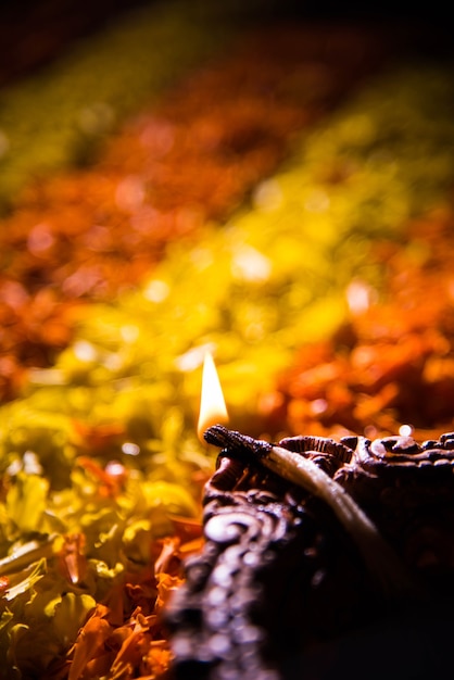 Diya tradicional o lámpara de aceite encendida en coloridos rangoli hechos de pétalos de flores, en el festival de luces llamado diwali o deepawali, enfoque selectivo