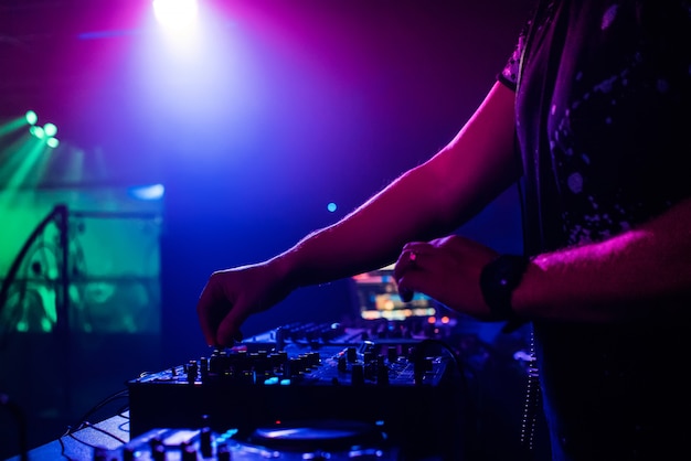 DJ en un club nocturno tocando en un mezclador profesional, focos que cambian de color