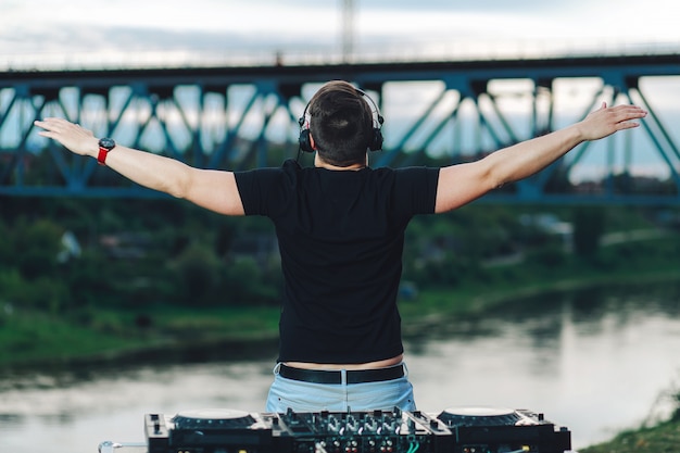 Foto dj de verdade toca música em uma festa, fica de costas, empurrando os braços para os lados ao ar livre