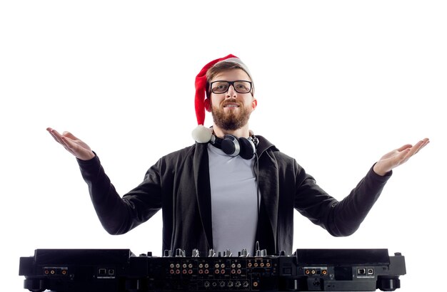 DJ feliz alegre barbudo com chapéu de Papai Noel e óculos toca música em uma plataforma giratória e levanta as mãos