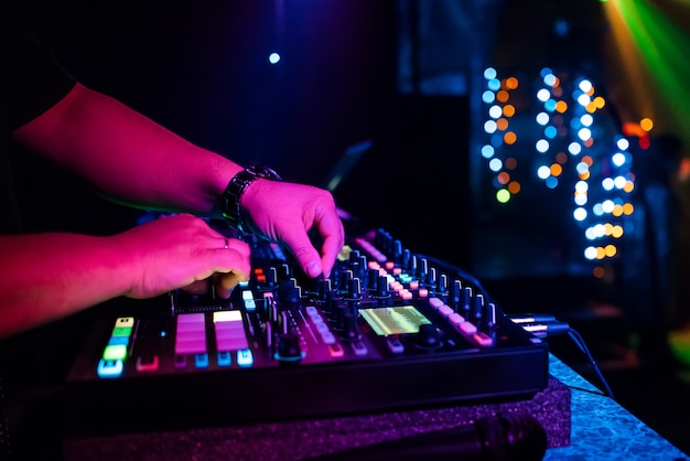 DJ masculino mezcla música electrónica con sus manos en un mezclador de música profesional