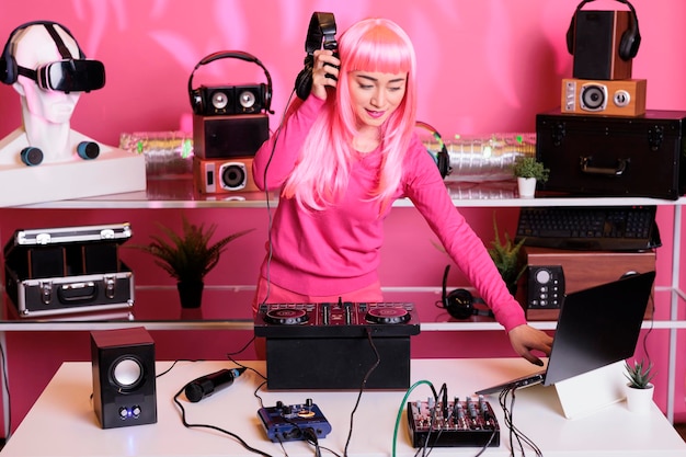 DJ mit rosa Haaren spielt elektronische Lieder an einer professionellen Mischkonsole, hört Musik über ein Headset und genießt das Nachtleben. Asiatischer Künstler hat Spaß im Club und tanzt während des Auftritts mit Fans
