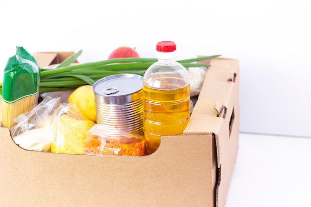 Doação. caixa de supermercado, ajude os produtos a quem precisa. caixa de doação. caixa de papelão com alimentos essenciais sobre uma superfície branca.