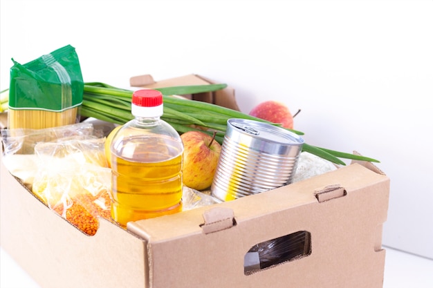 Doação. caixa de supermercado, ajude os produtos a quem precisa. caixa de doação. caixa de papelão com alimentos essenciais sobre uma superfície branca.