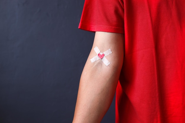 Doador de sangue em camiseta vermelha com bandagem depois de doar sangue em um fundo cinza Doação de sangue e