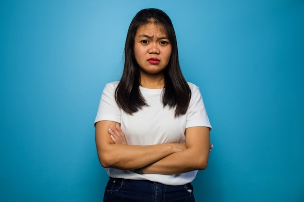 Doblar las manos y malhumorado de las mujeres asiáticas con camiseta blanca aislado sobre fondo azul.