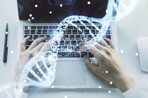 Doble exposición del holograma de ADN creativo y manos escribiendo en una computadora portátil en el concepto de investigación de ADN y bioingeniería de fondo
