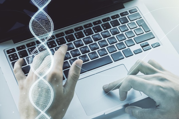 Doble exposición del holograma de ADN creativo y manos escribiendo en una computadora portátil en el concepto de investigación de ADN y bioingeniería de fondo