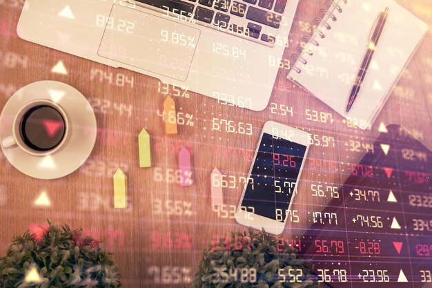 Doble exposición del holograma del gráfico financiero en el escritorio con el teléfono Vista superior Concepto de plataforma de comercio móvil