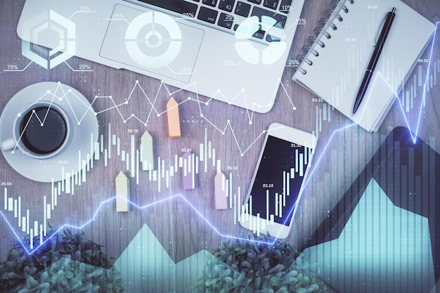 Doble exposición del holograma del gráfico financiero sobre el escritorio con el teléfono Vista superior Concepto de plataforma de comercio móvil