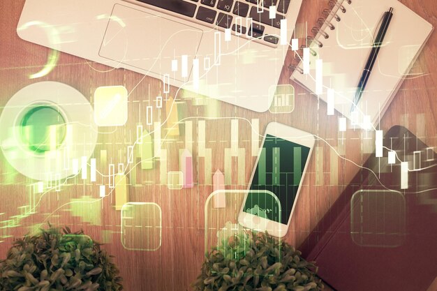 Doble exposición del holograma de gráficos financieros en el escritorio con el teléfono Vista superior Concepto de plataforma de comercio móvil