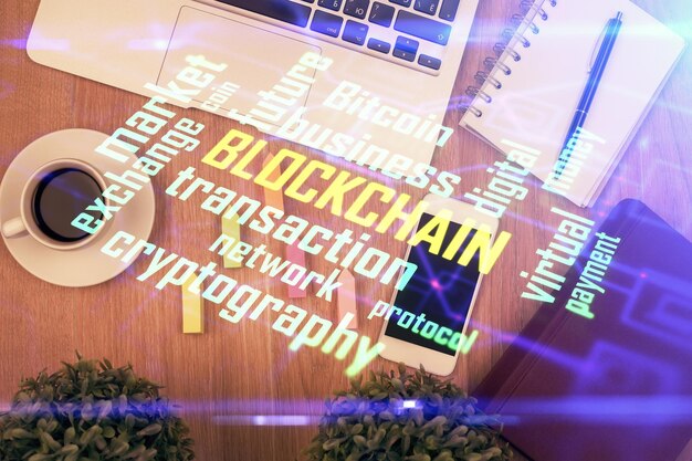 Doble exposición del holograma del tema blockchain sobre la mesa con el teléfono Vista superior Concepto de tecnología criptográfica