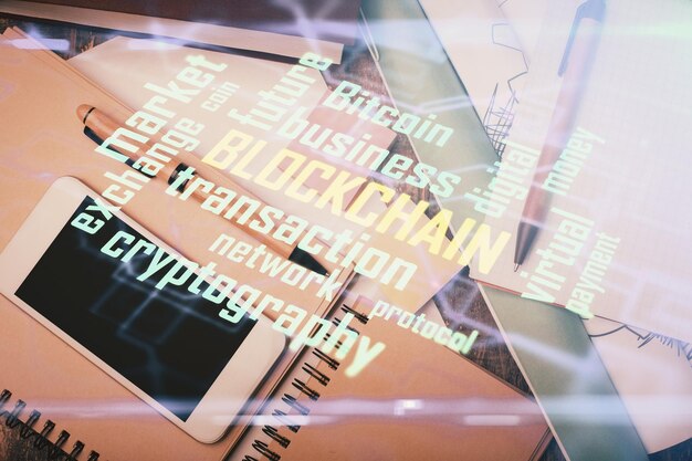 Doble exposición del holograma del tema blockchain sobre la mesa con el teléfono Vista superior Concepto de tecnología criptográfica