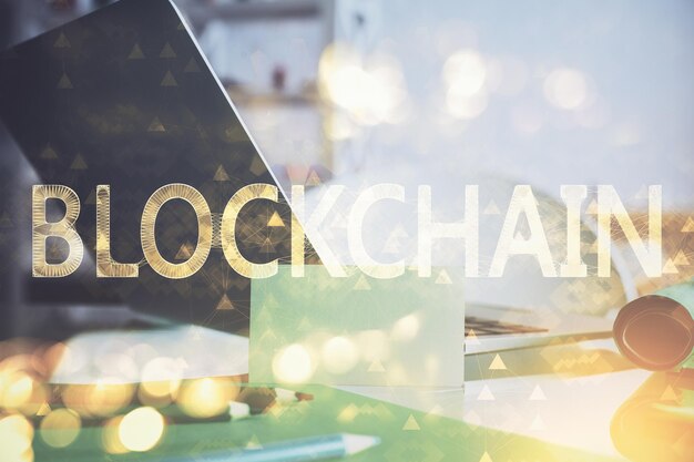 Doble exposición del holograma temático blockchain y criptoeconomía y mesa con fondo de computadora Concepto de criptomoneda bitcoin